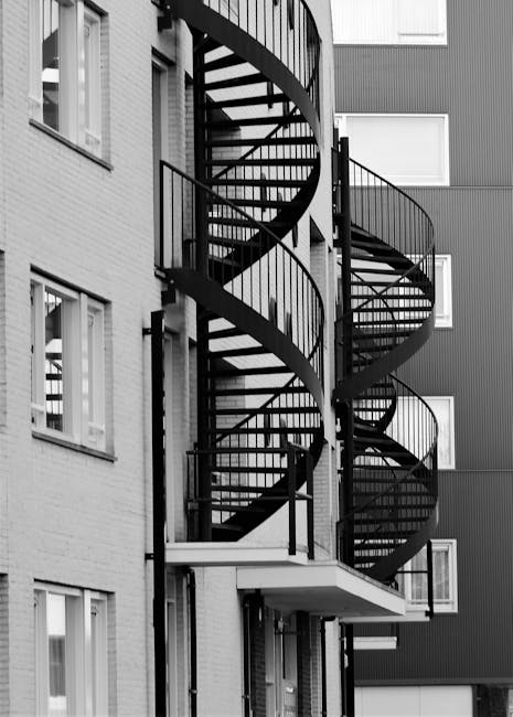 A top-down view of a staircase within a building, featuring metal handrails and steps made of gray tiles with a slightly textured surface. The steps are clean and free of debris, with some areas showi